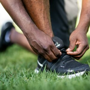 A man in athletic wear ties his sneakers on the grass, preparing for exercise outdoors.