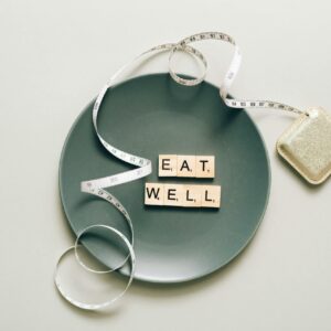 Flat lay of scrabble tiles spelling 'eat well' on a plate with a tape measure, promoting healthy eating.
